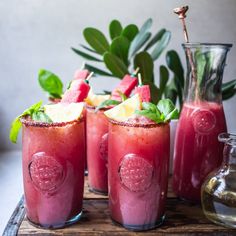 four glasses filled with red liquid and garnished with lemons, mint leaves and watermelon