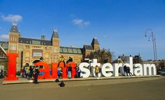 people standing in front of a large sign that says amsterdam on the side of a building