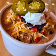 a white bowl filled with chili cheese soup and topped with sour cream, jalapenos