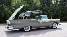 an old car with its hood open in a parking lot next to trees and bushes