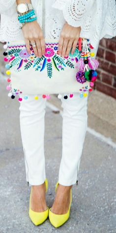 a woman holding a white purse with colorful pom poms