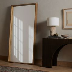 a room with a mirror, table and lamp on it in front of a wall