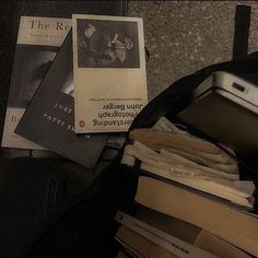 an open suitcase filled with books next to a pile of papers and other items on the floor