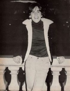 an old black and white photo of a young man leaning on a railing with his hands in his pockets