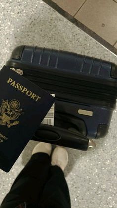 a person is holding a passport and standing next to a luggage bag on the floor