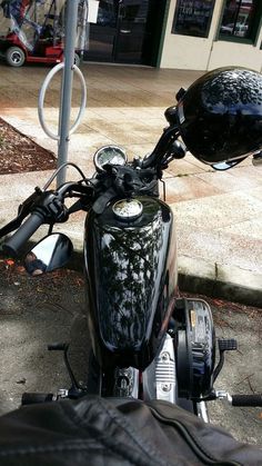 a black motorcycle parked next to a building on the side of a road with a helmet on it's handlebars