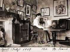 an old black and white photo of a woman sitting at a table in front of a fireplace