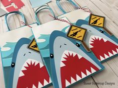 three shark bags with tags on them sitting on top of a wooden table next to paper cutouts