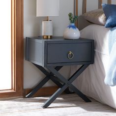 a nightstand with a lamp on top of it next to a bed