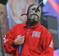 a man in a red jacket with a mask on holding a blue stick and wearing a black face mask