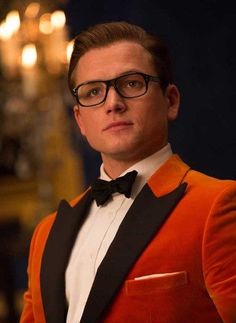 a man in an orange tuxedo and black bow tie looking at the camera