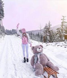 a woman standing next to a teddy bear on a sleigh in the snow