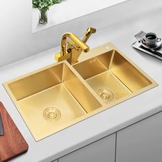 a kitchen sink with two gold faucets and a cutting board