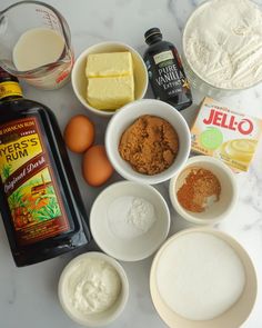 ingredients to make an orange cake laid out on a marble counter top, including eggs, flour, butter, sugar and syrup