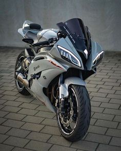 a silver and black motorcycle parked on top of a brick floor next to a wall