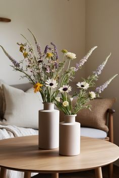 two vases with flowers are sitting on a coffee table in front of a couch