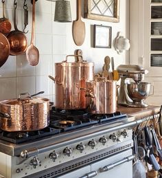 copper pots and pans are on the stove in this kitchen with white tile walls