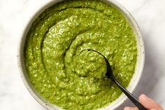 a hand holding a spoon over a bowl of guacamole