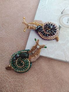 two pieces of jewelry sitting on top of a table next to a book with a clock in the background