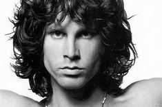 a black and white photo of a shirtless man with long curly hair wearing a necklace