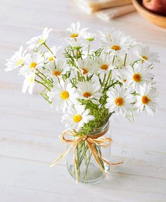 a vase filled with white daisies sitting on top of a table next to an apple