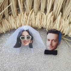 two cardboard cutouts of people wearing sunglasses and veils on the ground next to some straw