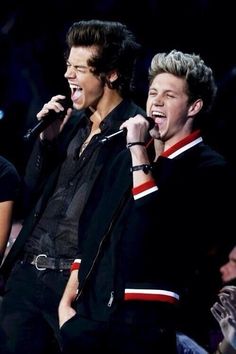 two men singing into microphones while standing next to each other in front of an audience