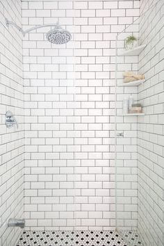 a white tiled shower with black and white floor tiles on the walls, along with shelves