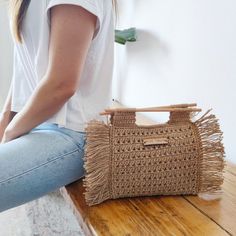 a woman sitting on the floor next to a straw bag with handles and fringes