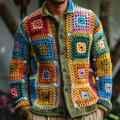 a man wearing a multicolored crocheted jacket and tan pants with his hands in his pockets