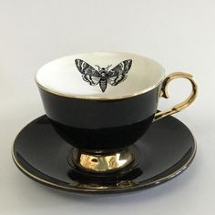 a black and white coffee cup with a butterfly on the side sitting on a saucer