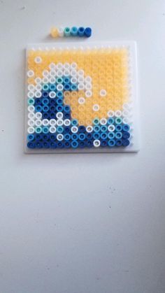 a piece of art made out of legos on a white surface with blue and yellow beads