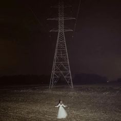 a woman standing in the middle of a field next to a power line at night