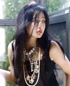 a woman with long black hair and necklaces standing in front of a glass window