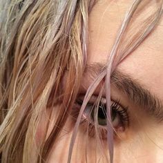 a close up of a person's eye with long hair blowing in the wind