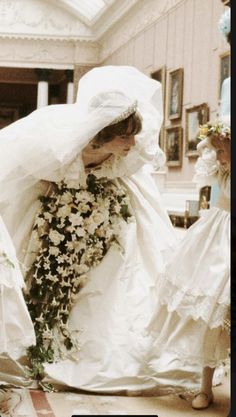 two women in white dresses and veils with flowers on the floor next to each other