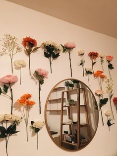 flowers are arranged on the wall behind a round mirror, with a shelf in front of it