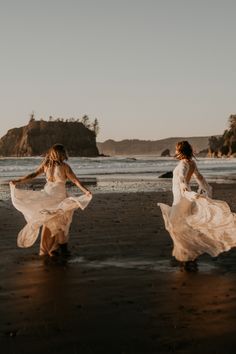 two women in white dresses are walking on the beach