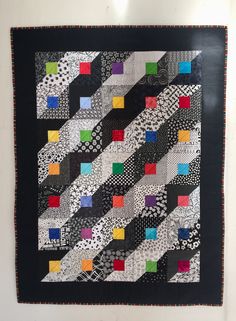 a black and white quilt hanging on the wall next to a wooden frame with colorful squares in it