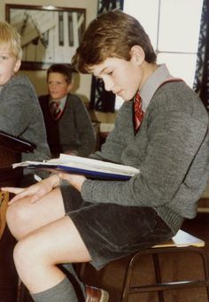 two young boys sitting at desks with books in their hands and one boy reading