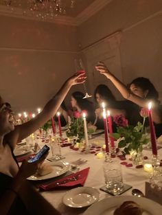 a group of people sitting around a dinner table with candles on it and plates in front of them