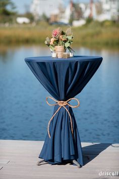 a table with a blue cloth draped over it and flowers tied to the top, sitting on a dock