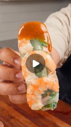 a person holding up a piece of sushi with sauce on the top and shrimp in the middle