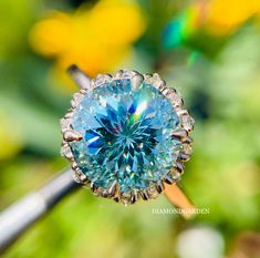 a blue diamond ring sitting on top of a wooden stick in front of yellow flowers