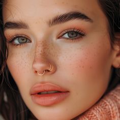 a woman with freckles on her nose wearing a gold nose ring and piercing