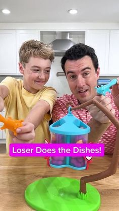 a man and boy are playing with toys on the kitchen counter top that says, loser does the dishes