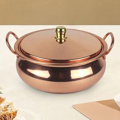 a large copper pot sitting on top of a table next to a plate with food