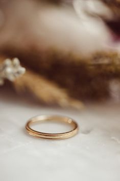 a gold wedding band sitting on top of a white table next to some dried flowers