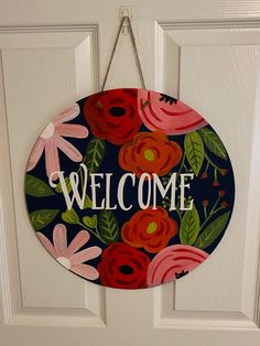 a welcome sign hanging on the front door with flowers and leaves painted on it's side