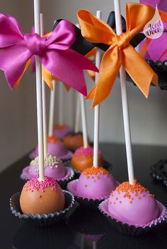 some cake pops with pink frosting and orange sprinkles are on a black table